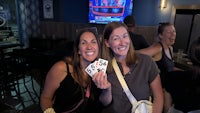 two women holding up playing cards in a bar
